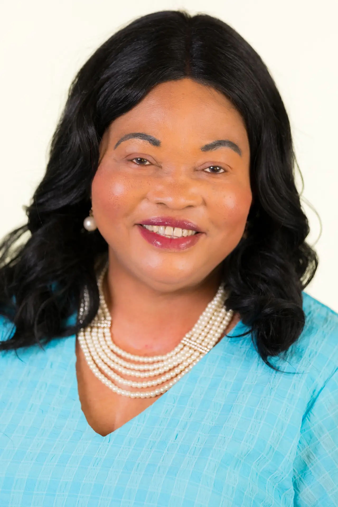 Close-up portrait of a smiling woman with dark hair, wearing a turquoise top and pearl necklace.