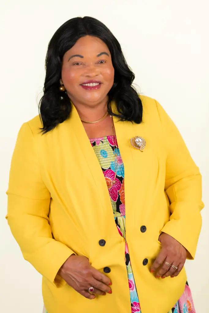 Smiling woman in a bright yellow blazer with a colorful dress, posing against a light background.